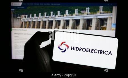 Stoccarda, Germania, 06-30-2023: Persona che detiene il cellulare con il logo della società energetica rumena Hidroelectrica SA sullo schermo davanti all'azienda Foto Stock