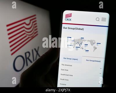 Stoccarda, Germania, 07-01-2023: Persona che detiene il cellulare con pagina web della società finanziaria giapponese ORIX Corporation sullo schermo davanti al logo. Foto Stock