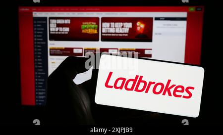 Stoccarda, Germania, 06-30-2023: Persona che detiene il cellulare con il logo della società LC International Limited (Ladbrokes) sullo schermo davanti alla pagina web. Foto Stock