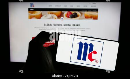 Stoccarda, Germania, 07-08-2023: Persona che detiene il cellulare con il logo della società statunitense McCormick Company incorporata sullo schermo davanti all'azienda Foto Stock
