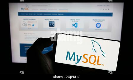 Stoccarda, Germania, 07-13-2023: Persona che tiene un cellulare con il logo del sistema di gestione di database relazionali MySQL sullo schermo davanti alla pagina web. Foto Stock