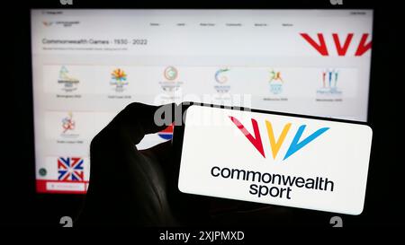 Stoccarda, Germania, 07-30-2023: Persona che tiene il cellulare con il logo dell'organizzazione Commonwealth Games Federation (CGF) sullo schermo davanti alla pagina web. Foto Stock