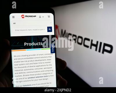 Stoccarda, Germania, 08-04-2023: Persona che detiene un telefono cellulare con pagina web della società di semiconduttori Microchip Technology Inc. Su schermo con logo. Foto Stock