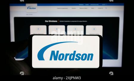 Stoccarda, Germania, 08-06-2023: Persona che detiene il cellulare con il logo della società di distribuzione statunitense Nordson Corporation sullo schermo davanti all'azienda Foto Stock