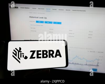 Stoccarda, Germania, 08-13-2023: Persona che detiene un telefono cellulare con il logo della società americana Zebra Technologies Corporation sullo schermo davanti al Web Foto Stock