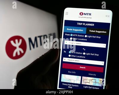 Stoccarda, Germania, 08-16-2023: Persona che detiene il cellulare con pagina web della compagnia ferroviaria cinese MTR Corporation Limited sullo schermo con logo. Concentrati su Foto Stock