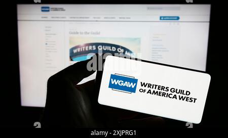 Stoccarda, Germania, 08-26-2023: Persona che tiene il cellulare con il logo del sindacato Writers Guild of America West (WGAW) sullo schermo davanti alla pagina web. Foto Stock