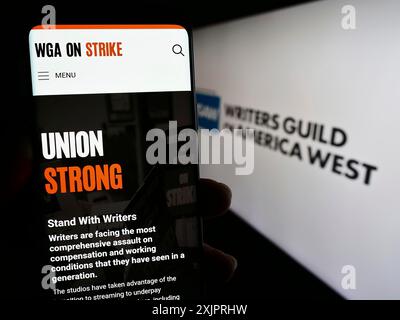 Stoccarda, Germania, 08-26-2023: Persona che tiene in mano lo smartphone con pagina web del sindacato Writers Guild of America West (WGAW) sullo schermo con logo. Foto Stock