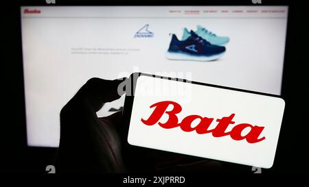 Stoccarda, Germania, 08-29-2023: Persona che detiene il cellulare con il logo della società di calzature Bata Corporation sullo schermo di fronte alla pagina web aziendale. Concentrati Foto Stock