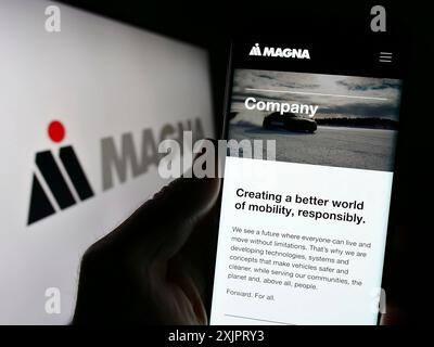 Stoccarda, Germania, 08-29-2023: Persona che detiene il cellulare con il sito web dell'azienda automobilistica Magna International Inc. Sullo schermo davanti al logo. Foto Stock