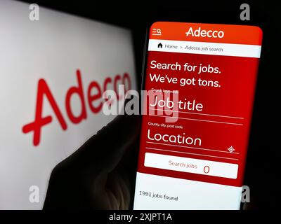 Stoccarda, Germania, 09-02-2023: Persona che detiene il cellulare con pagina web della società di reclutamento Adecco sullo schermo davanti al logo aziendale. Concentrati su Foto Stock