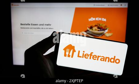 Stoccarda, Germania, 09-10-2023: Persona in possesso di uno smartphone con logo della società di consegna di prodotti alimentari tedesca Lieferando sullo schermo di fronte al sito web. Concentrati Foto Stock