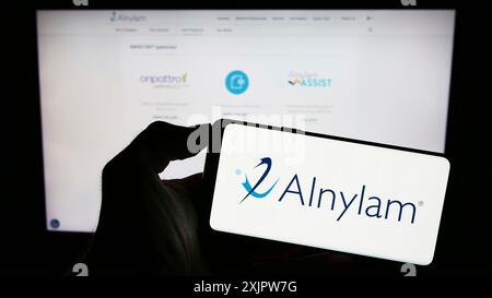 Stoccarda, Germania, 09-20-2023: Persona che detiene il cellulare con il logo della società statunitense Alnylam Pharmaceuticals Inc. Sullo schermo di fronte alla pagina web aziendale. Foto Stock