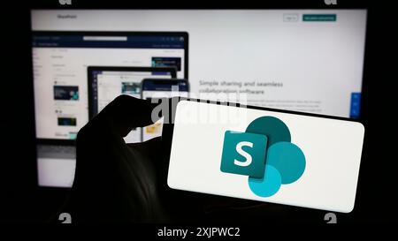 Stoccarda, Germania, 09-21-2023: Persona che tiene in mano uno smartphone con logo della piattaforma collaborativa Microsoft SharePoint sullo schermo di fronte al sito Web. Foto Stock