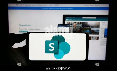 Stoccarda, Germania, 09-21-2023: Persona che tiene il cellulare con il logo della piattaforma collaborativa Microsoft SharePoint sullo schermo di fronte all'azienda Foto Stock