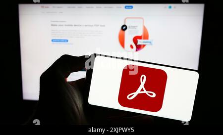 Stoccarda, Germania, 09-23-2023: Persona che tiene un cellulare con il logo del software di gestione PDF Adobe Acrobat sullo schermo di fronte alla pagina web aziendale. Foto Stock