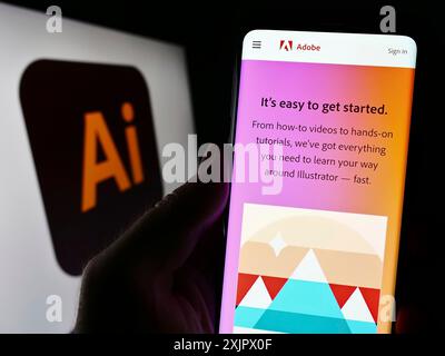 Stoccarda, Germania, 09-23-2023: Persona che tiene il cellulare con pagina web dell'editor di grafica vettoriale Adobe Illustrator sullo schermo davanti al logo. Concentrati Foto Stock