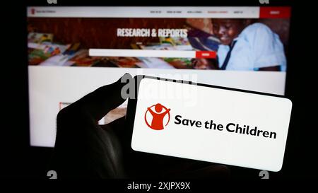 Stoccarda, Germania, 10-06-2023: Persona che detiene un telefono cellulare con il logo dell'organizzazione benefica Save the Children Fund davanti alla pagina web. Concentrati su Foto Stock