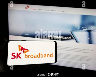 Stoccarda, Germania, 10-16-2023: Persona con smartphone con logo della società di telecomunicazioni coreana SK Broadband Inc. Davanti al sito web. Concentrati Foto Stock