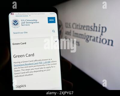 Stoccarda, Germania, 10-29-2023: Persona che possiede un telefono cellulare con pagina web dell'agenzia statunitense Citizenship and Immigration Services (USCIS) con sigillo. Concentrati Foto Stock