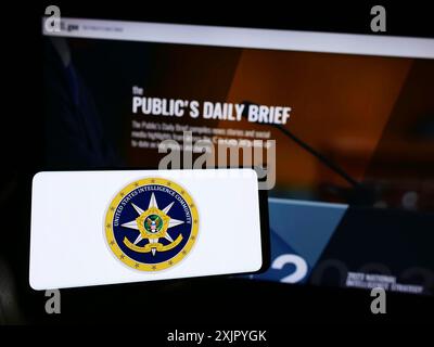 Stoccarda, Germania, 10-29-2023: Persona che detiene il cellulare con il sigillo del gruppo di agenzie United States Intelligence Community (IC) di fronte alla pagina web. Foto Stock