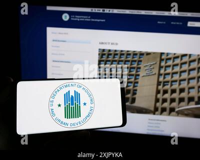 Stoccarda, Germania, 10-30-2023: Persona con smartphone con logo del Dipartimento degli alloggi e dello sviluppo urbano (HUD) degli Stati Uniti davanti al sito web. Foto Stock