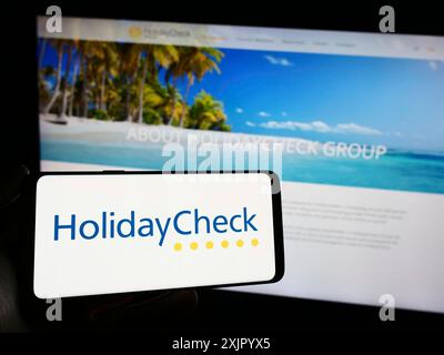 Stoccarda, Germania, 11-02-2023: Persona che detiene un cellulare con il logo della società svizzera HolidayCheck AG del portale di prenotazione viaggi di fronte all'azienda Foto Stock