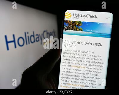 Stoccarda, Germania, 11-02-2023: Persona in possesso di smartphone con pagina web della società svizzera HolidayCheck AG del portale di prenotazione viaggi davanti al logo. Concentrati Foto Stock