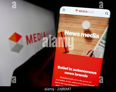 Stoccarda, Germania, 11-10-2023: Persona che detiene il cellulare con pagina web della società mediatica belga Mediahuis NV davanti al logo aziendale. Concentrati su Foto Stock