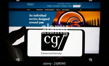 Stoccarda, Germania, 11-11-2023: Persona che possiede uno smartphone con logo della società finanziaria canadese Canaccord Genuity Group Inc. Davanti al sito Web. Foto Stock