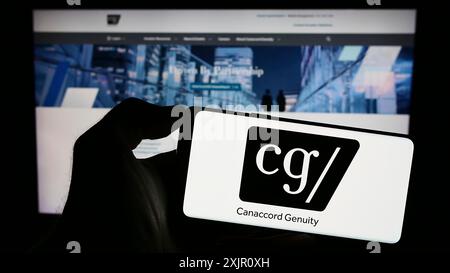 Stoccarda, Germania, 11-11-2023: Persona che detiene il cellulare con il logo della società finanziaria canadese Canaccord Genuity Group Inc. Davanti alla pagina web. Foto Stock