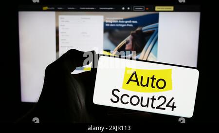 Stoccarda, Germania, 11-14-2023: Persona che detiene il cellulare con il logo della società tedesca AutoScout24 GmbH, sul mercato automobilistico online, davanti alla pagina web. Foto Stock