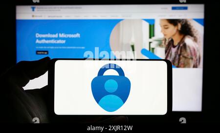 Stoccarda, Germania, 11-14-2023: Persona che possiede un telefono cellulare con il logo dell'app di autenticazione Microsoft Authenticator davanti alla pagina Web aziendale. Foto Stock