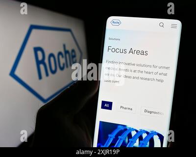 Stoccarda, Germania, 11-16-2023: Persona che detiene il cellulare con pagina web della società sanitaria svizzera Roche Holding AG davanti al logo aziendale. Concentrati Foto Stock