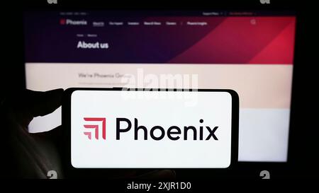 Stoccarda, Germania, 11-17-2023: Persona che detiene il cellulare con il logo della compagnia assicurativa britannica Phoenix Group Holdings plc davanti all'azienda Foto Stock