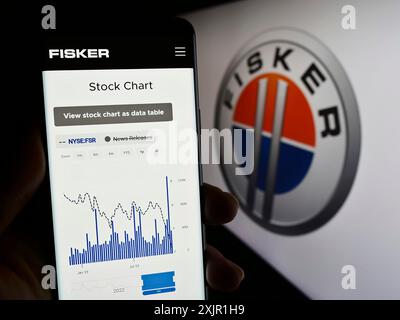 Stoccarda, Germania, 11-21-2023: Persona che possiede uno smartphone con pagina Web della società statunitense di veicoli elettrici Fisker Inc. Davanti al logo aziendale. Concentrati Foto Stock