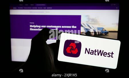 Stoccarda, Germania, 11-22-2023: Persona che detiene il cellulare con il logo della società finanziaria National Westminster Bank (NatWest) di fronte all'azienda Foto Stock