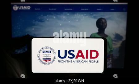 Stoccarda, Germania, 11-27-2023: Persona che tiene lo smartphone con il sigillo della United States Agency for International Development (USAID) di fronte Foto Stock