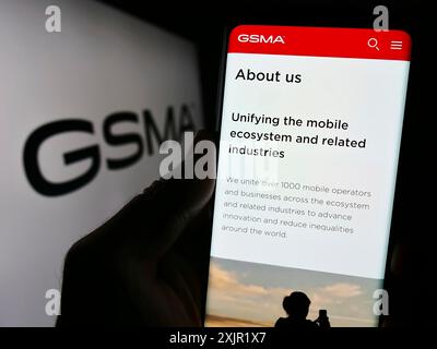 Stoccarda, Germania, 11-27-2023: Persona che detiene un cellulare con pagina web dell’organizzazione del settore mobile GSM Association (GSMA) davanti al logo. Concentrati Foto Stock