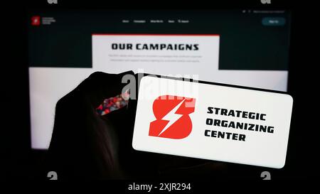 Stoccarda, Germania, 11-29-2023: Persona che tiene un telefono cellulare con il logo del Centro organizzativo strategico della coalizione sindacale (SOC) di fronte al web Foto Stock