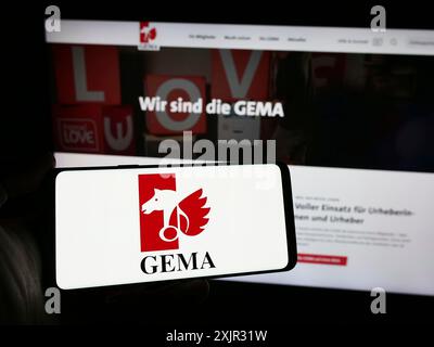 Stoccarda, Germania, 12-14-2023: Persona in possesso di smartphone con logo della società tedesca di gestione collettiva GEMA davanti al sito web. Mettere a fuoco il display del telefono Foto Stock