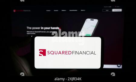 Stoccarda, Germania, 12-15-2023: Persona che detiene il cellulare con il logo della società di piattaforme commerciali SquaredFinancial davanti alla pagina web aziendale. Concentrati Foto Stock