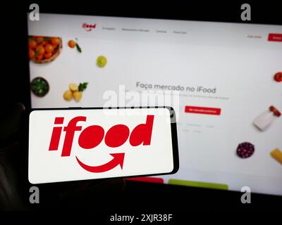 Stoccarda, Germania, 12-18-2023: Persona con smartphone con logo della società brasiliana di ordinazione e consegna di prodotti alimentari iFood davanti al sito web. Concentrati Foto Stock
