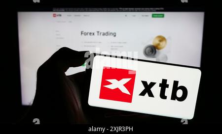 Stoccarda, Germania, 12-22-2023: Persona che detiene il cellulare con il logo della società polacca di intermediazione d’investimento XTB S.A. di fronte alla pagina web aziendale. Concentrati Foto Stock