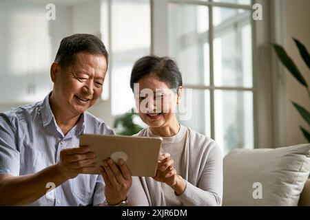 felice coppia asiatica anziana seduta sul divano a casa usando un tablet digitale insieme Foto Stock