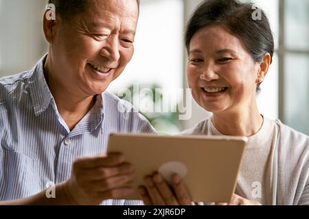 felice coppia asiatica anziana seduta sul divano a casa usando un tablet digitale insieme Foto Stock