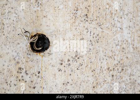 Fili elettrici sporgenti dal foro della presa elettrica rotto sulla parete in cemento di colore beige Foto Stock