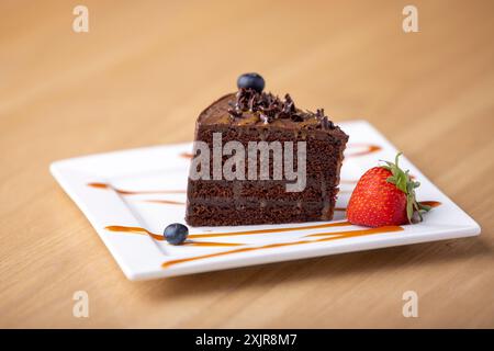 Una deliziosa fetta di ricca torta al cioccolato condita con caramello e ricoperta di scaglie di cioccolato e mirtillo, accompagnata da fragole fresche. Foto Stock