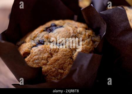 Muffin con gocce di cioccolato alla banana appena sfornati avvolti in carta pergamena marrone, posti su un tagliere di legno accanto a un mucchio di banane mature. Foto Stock