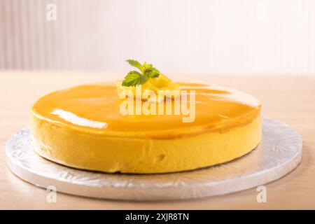 Una cheesecake di mango finemente smaltata con una dose di purea di mango e foglie di menta fresca. La torta viene presentata su una tavola da torta d'argento Foto Stock